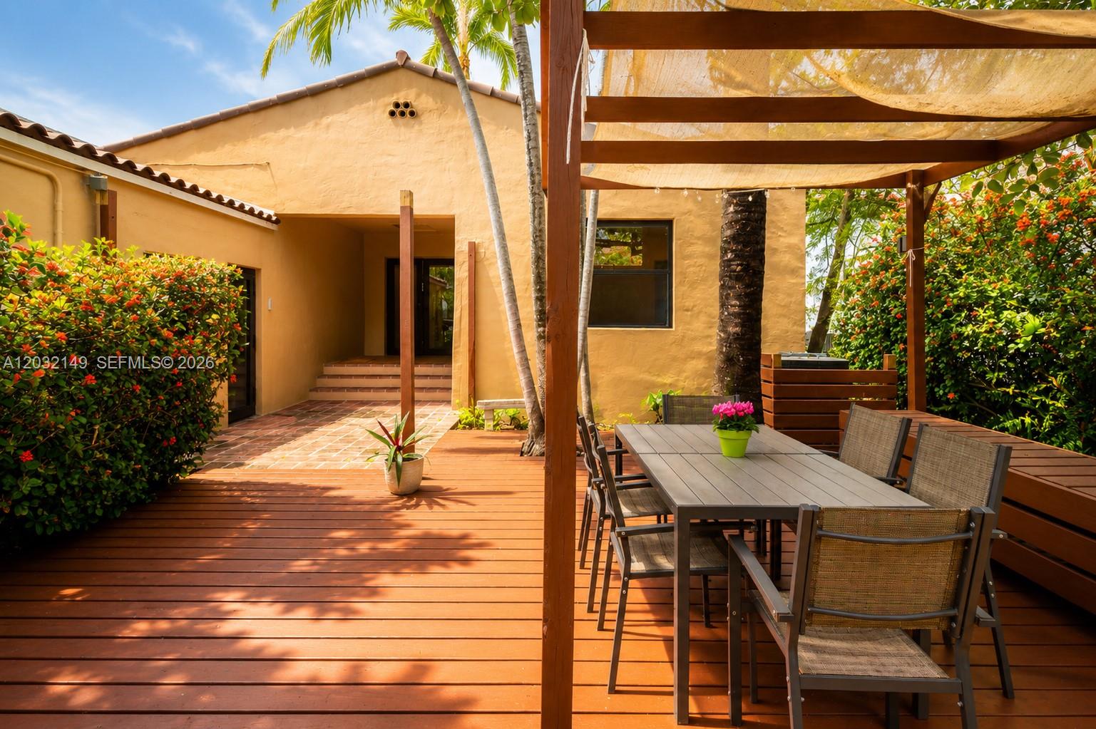 A wooden deck features a dining set under a pergola next to a stucco house — 4230 Royal Palm Ave, Miami Beach FL 33140, MIAMI BEACH, FL