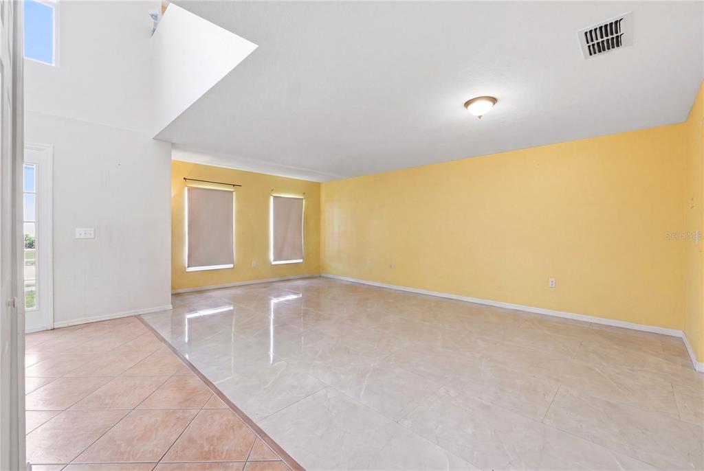 An empty room features yellow walls, light-colored tile flooring, and two windows with shades — 177 FISH HAWK DRIVE, WINTER HAVEN, FL