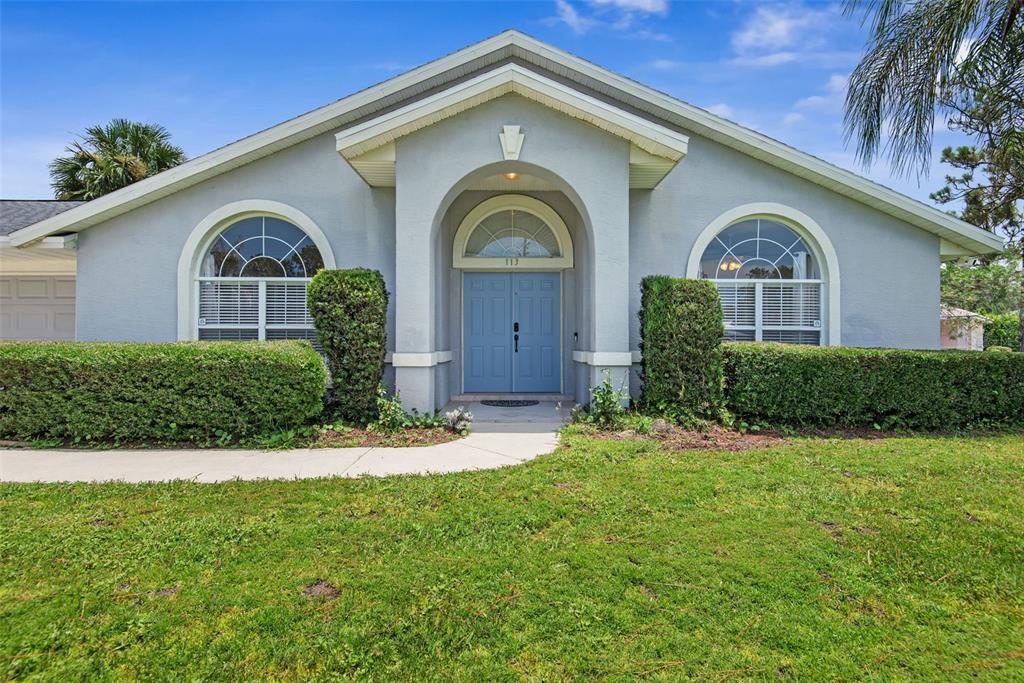 A single-story house with a blue front door, arched windows, and a manicured hedge — 113 WHIPPOORWILL DRIVE, PALM COAST, FL