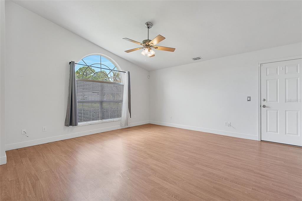 An empty room with light wood-look flooring, white walls, a ceiling fan, and arched window — 113 WHIPPOORWILL DRIVE, PALM COAST, FL