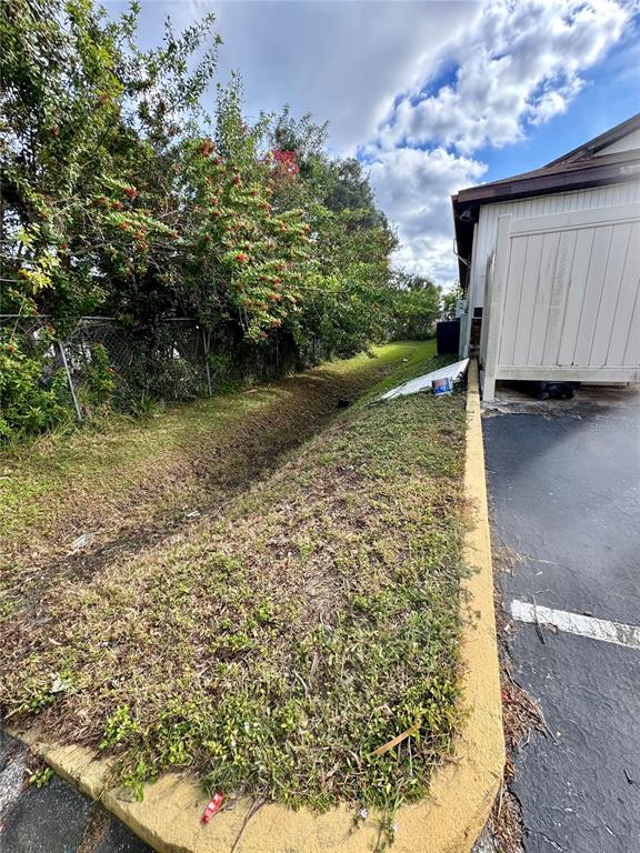 A grassy drainage ditch runs alongside a paved parking area and a white privacy fence — 2335 S RIDGEWOOD AVENUE, SOUTH DAYTONA, FL