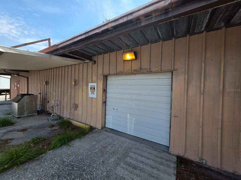 An exterior view of a tan metal building with a white roll-up garage door — 3603 W BEARSS AVENUE, TAMPA, FL