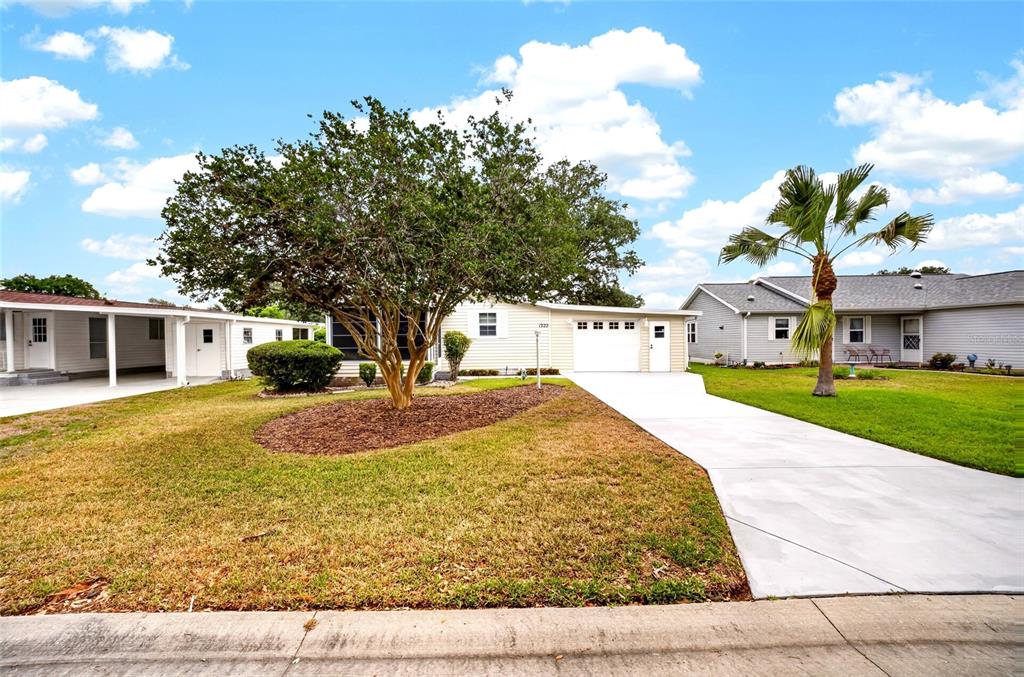 A single-story house with a white garage, a large tree, and a palm tree — 1222 ZAPATA PLACE, LADY LAKE, FL