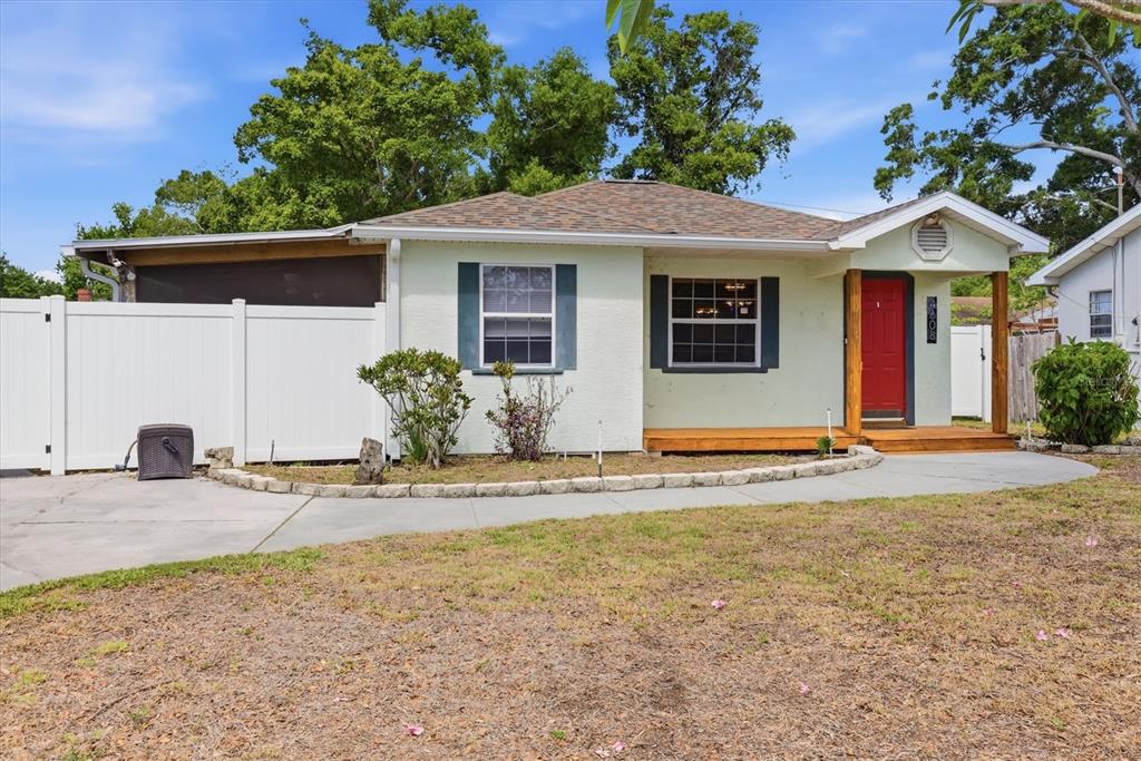 A light-colored single-story house features a red front door, a wooden porch, and white fencing — 4608 46TH STREET N, ST PETERSBURG, FL