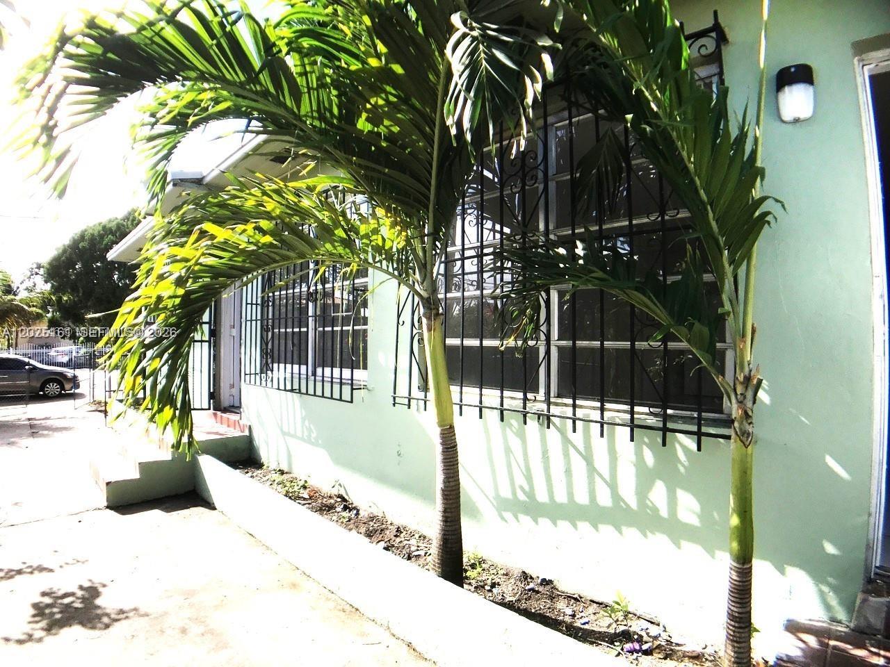 A light green house exterior features palm trees and windows covered with black security bars — 1321 NW 28th St, Miami FL 33142, MIAMI, FL
