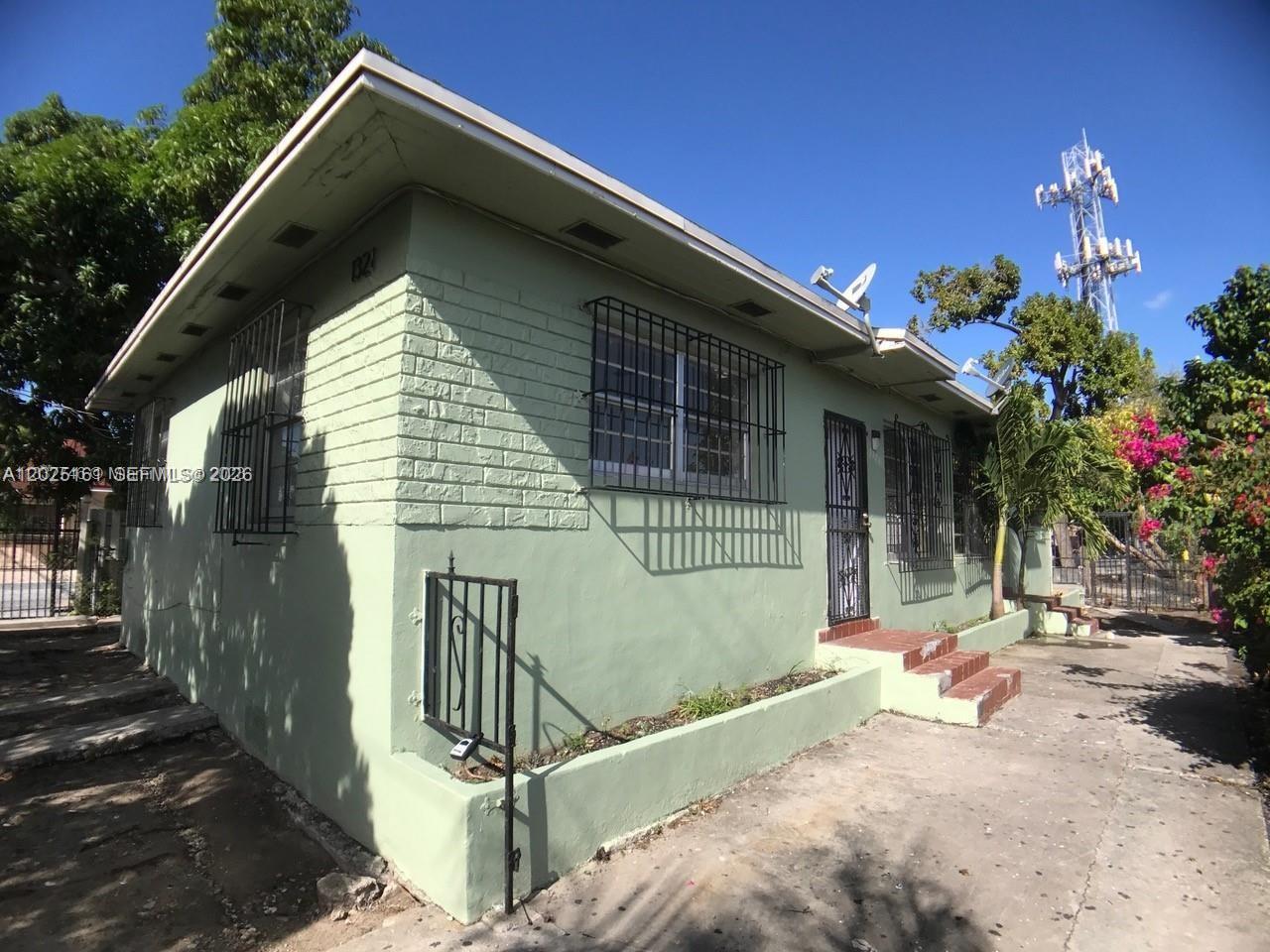 A light green, single-story house with a brick exterior, security bars, and a concrete driveway — 1321 NW 28th St, Miami FL 33142, MIAMI, FL