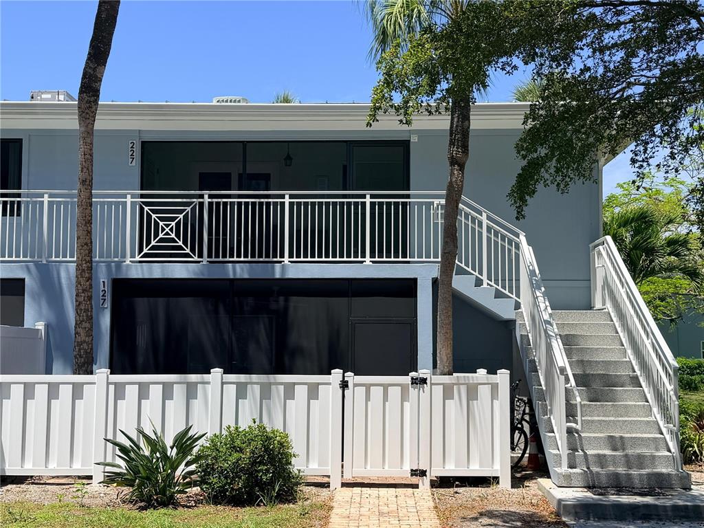 A two-story blue building features a white balcony, a ground-level patio, and an outdoor staircase — 600 MANATEE AVENUE UNIT 227, BRADENTON BEACH, FL
