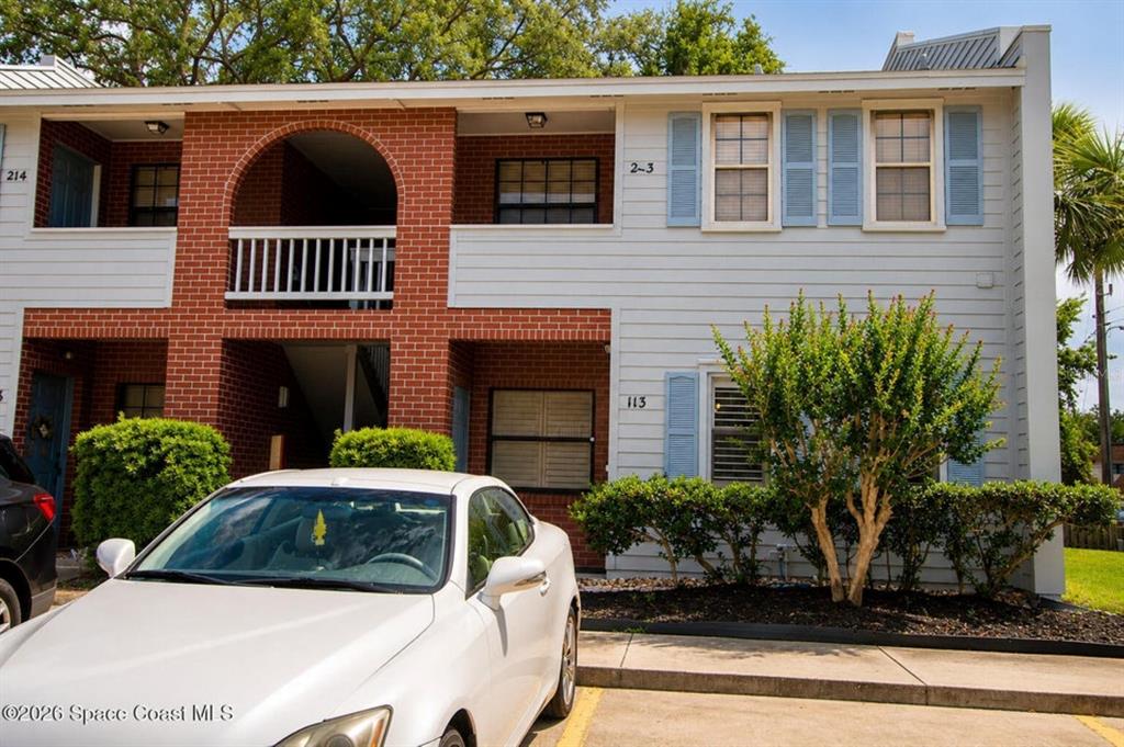 A two-story apartment building features a brick facade, light-colored siding, and a white car parked — 1795 HARRISON STREET UNIT 213, TITUSVILLE, FL