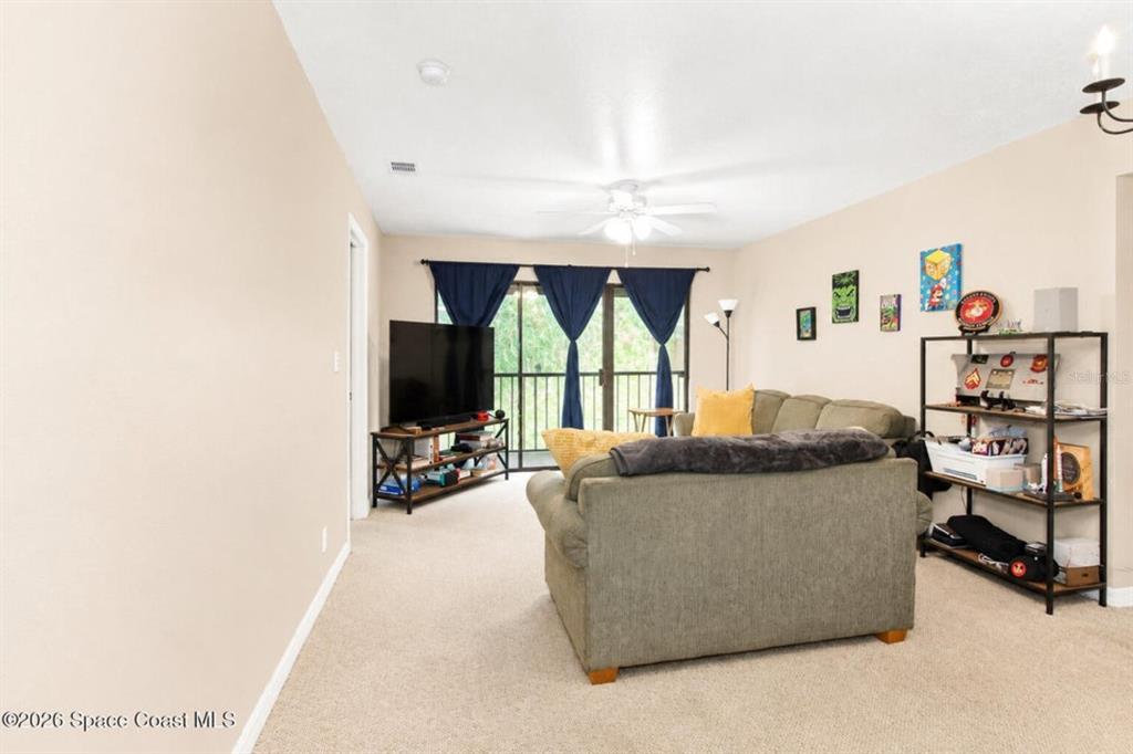 This living room features beige carpet, a ceiling fan, a sofa, and a television stand — 1795 HARRISON STREET UNIT 213, TITUSVILLE, FL