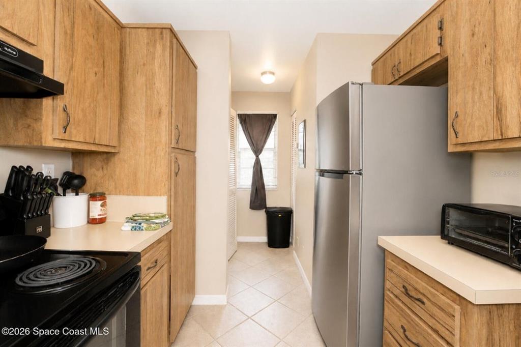 A galley kitchen features wood-grain cabinets, light countertops, stainless steel appliances, and tile flooring — 1795 HARRISON STREET UNIT 213, TITUSVILLE, FL
