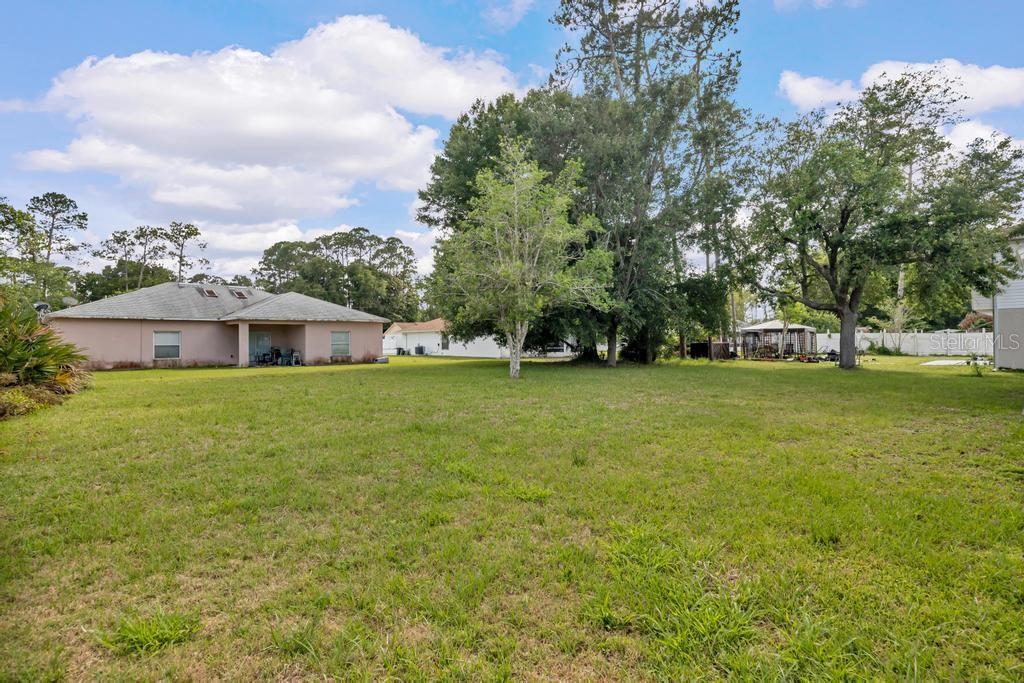 A large, grassy backyard features a single-story house, several mature trees, and a small gazebo — 62 BELVEDERE LANE, PALM COAST, FL