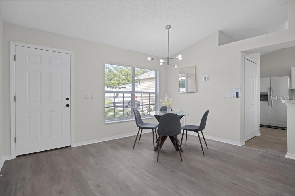 A dining area features gray wood-look flooring, a modern chandelier, and a glass-topped table — 62 BELVEDERE LANE, PALM COAST, FL