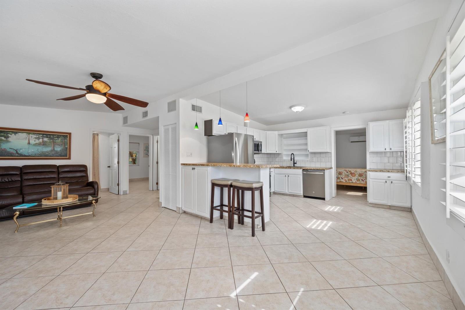 An open-concept living room and kitchen with tile flooring, white cabinets, and a breakfast bar — 2179 Pepper Road, West Palm Beach FL 33415, WEST PALM BEACH, FL