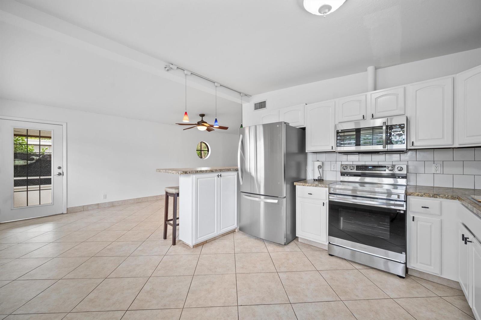 A kitchen with white cabinets, stainless steel appliances, and a breakfast bar on tile flooring — 2179 Pepper Road, West Palm Beach FL 33415, WEST PALM BEACH, FL