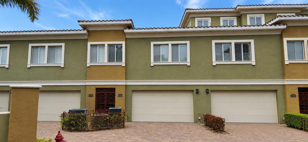 A multi-story townhouse exterior features olive green stucco walls, beige garage doors, and a paver driveway — 4907 BAYSHORE BOULEVARD UNIT 103, TAMPA, FL