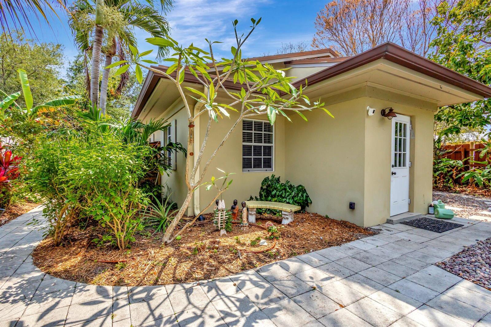 A tan exterior wall of a house features a white door and a small garden — 227 NE 12th Street # 1, Delray Beach FL 33444, DELRAY BEACH, FL