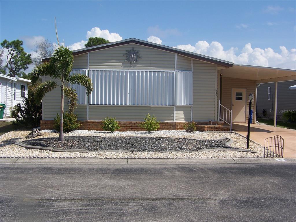 A single-story manufactured home with light siding, a front carport, and a landscaped rock yard — 15550 BURNT STORE ROAD UNIT 101, PUNTA GORDA, FL