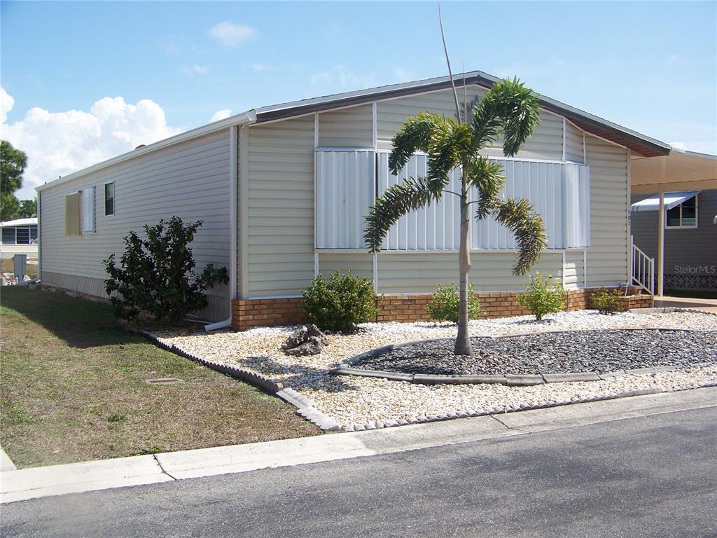 A beige manufactured home features a palm tree, brick skirting, and white storm shutters — 15550 BURNT STORE ROAD UNIT 101, PUNTA GORDA, FL
