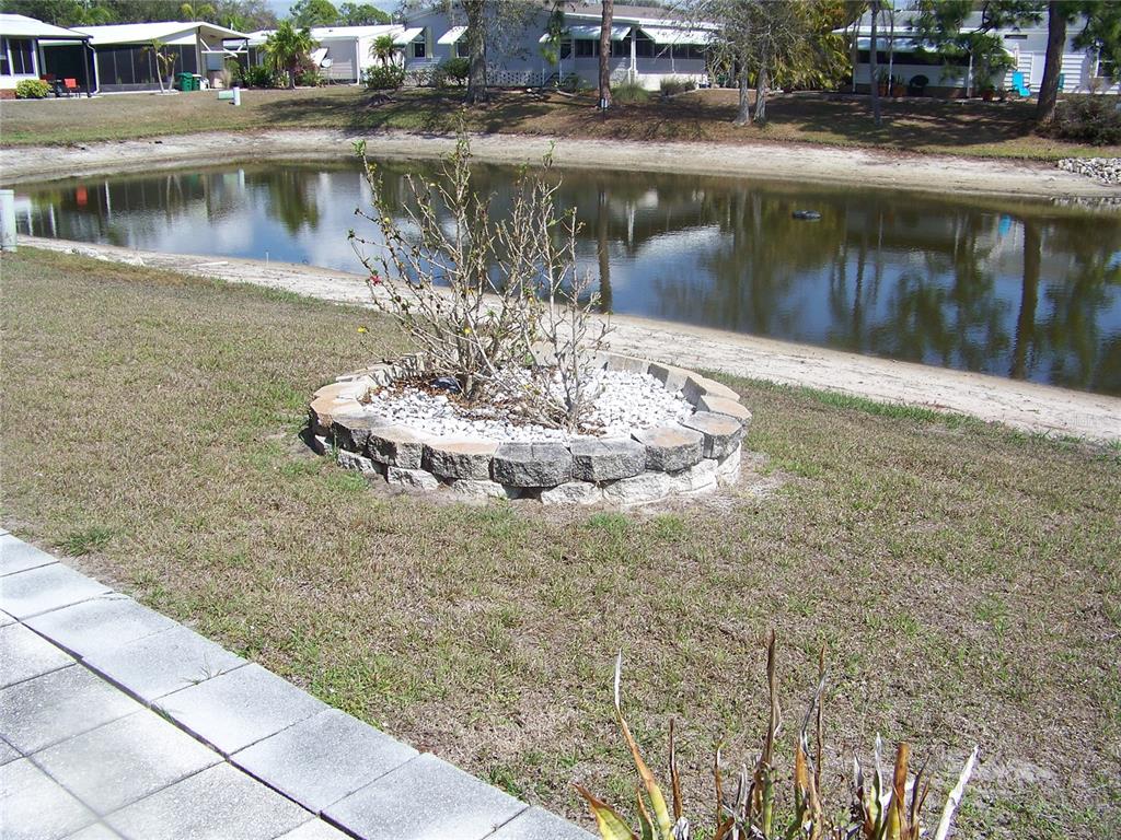 A circular stone planter sits in a grassy yard overlooking a small pond — 15550 BURNT STORE ROAD UNIT 101, PUNTA GORDA, FL