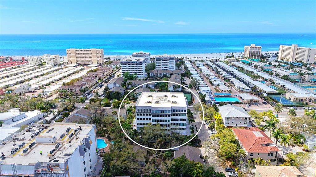 An aerial view shows a multi-story apartment building surrounded by coastal residential properties and beaches — 1200 EAST PEPPERTREE LANE UNIT 302, SARASOTA, FL