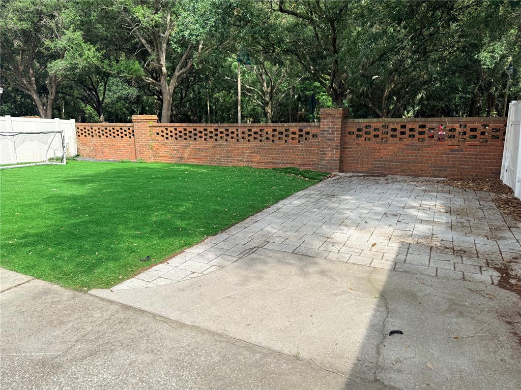 A backyard features a brick wall, a paved patio area, and a patch of artificial turf — 603 CANNE PLACE, CELEBRATION, FL