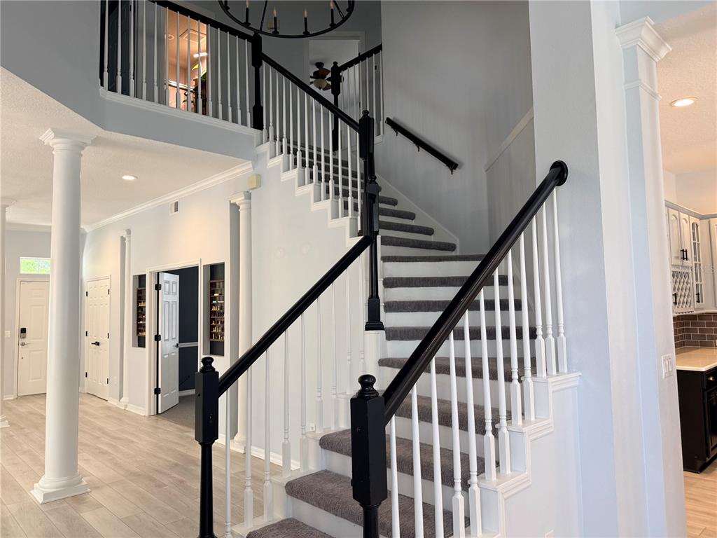 A foyer features a carpeted staircase with black railings and white balusters under a chandelier — 603 CANNE PLACE, CELEBRATION, FL