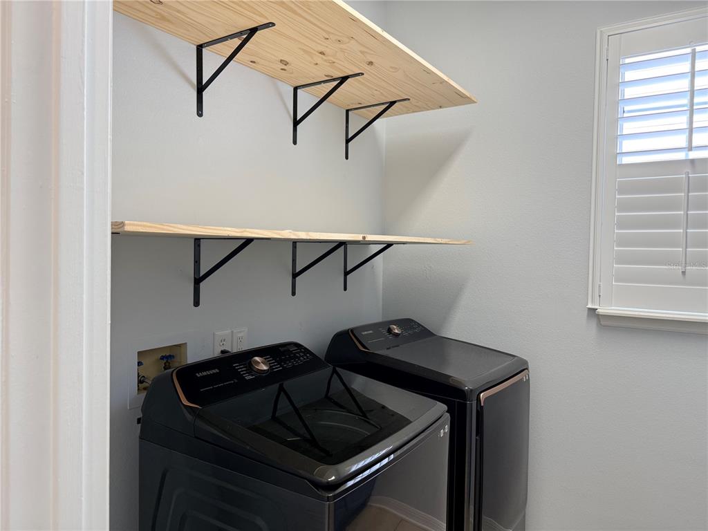 A laundry room features two wooden shelves mounted above black Samsung washer and dryer units — 603 CANNE PLACE, CELEBRATION, FL
