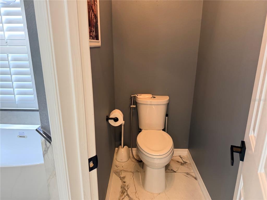 A small bathroom features a white toilet, gray walls, and white marble-look floor tiles — 603 CANNE PLACE, CELEBRATION, FL