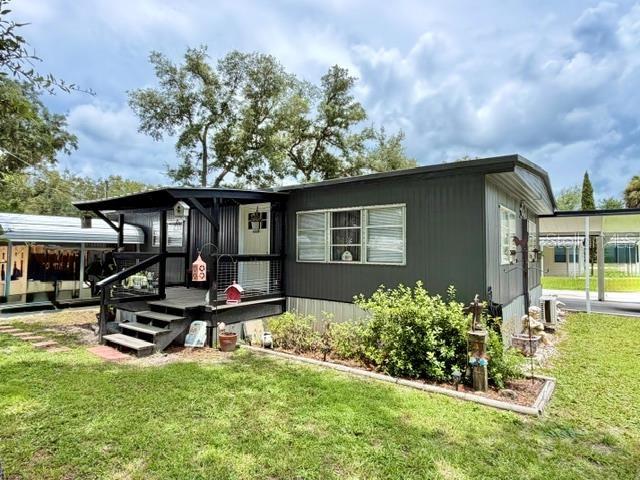 A dark-sided mobile home features a wooden front porch and a small landscaped garden area — 11097 NW 114TH STREET, CHIEFLAND, FL