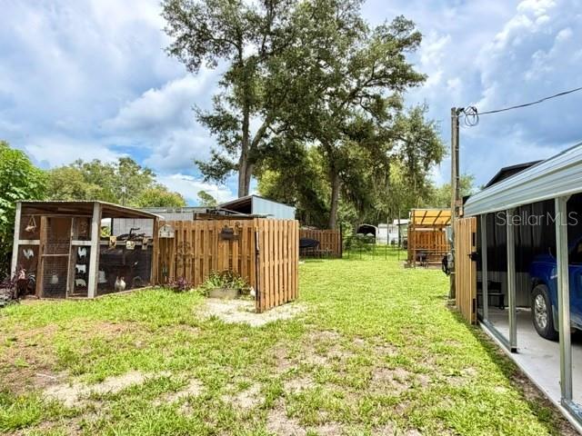 A backyard features a chicken coop, a wooden fence, and a metal carport structure — 11097 NW 114TH STREET, CHIEFLAND, FL