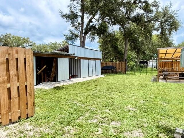 A metal-sided storage building stands in a grassy backyard next to a wooden fence — 11097 NW 114TH STREET, CHIEFLAND, FL