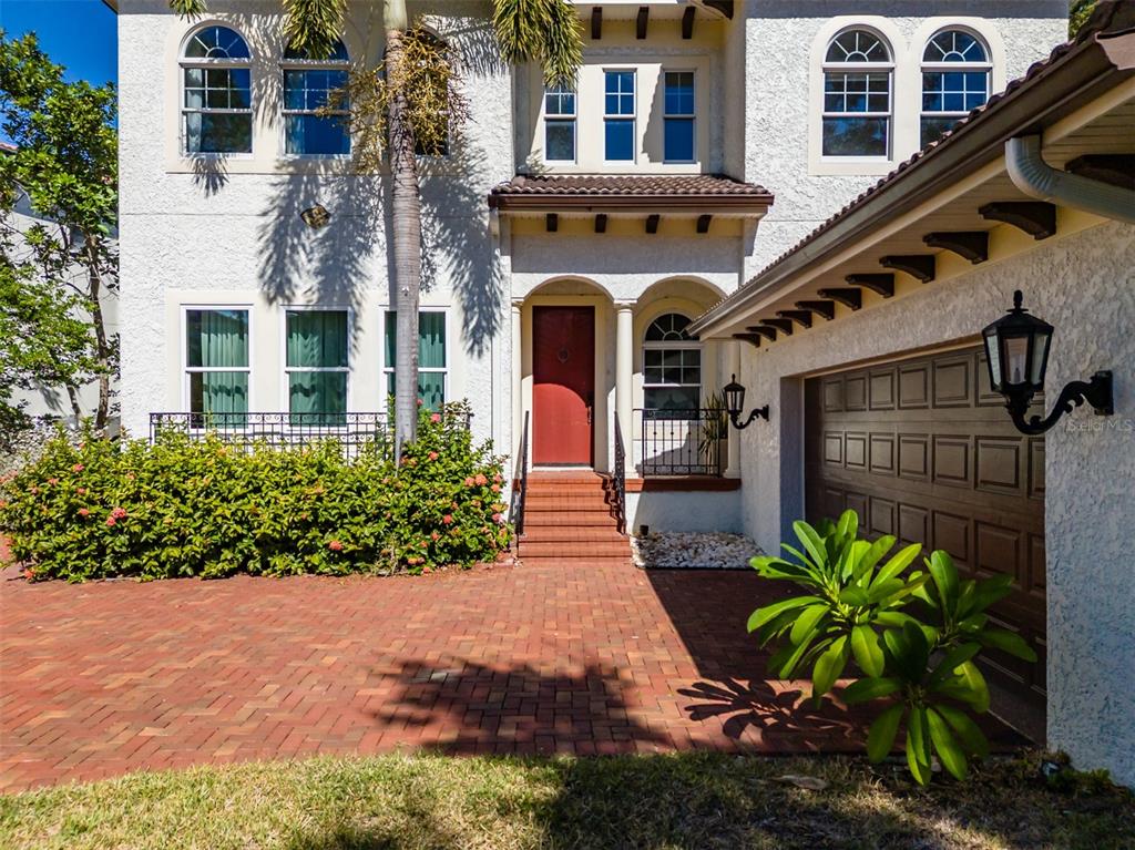 The exterior of a two-story home features a red front door, brick driveway, and garage — 4605 W VASCONIA STREET, TAMPA, FL