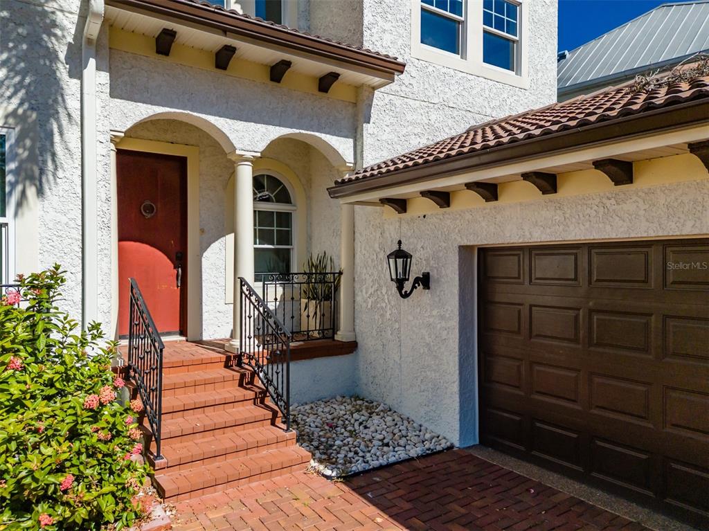 A stucco house exterior features a red door, brick steps, and a brown garage door — 4605 W VASCONIA STREET, TAMPA, FL