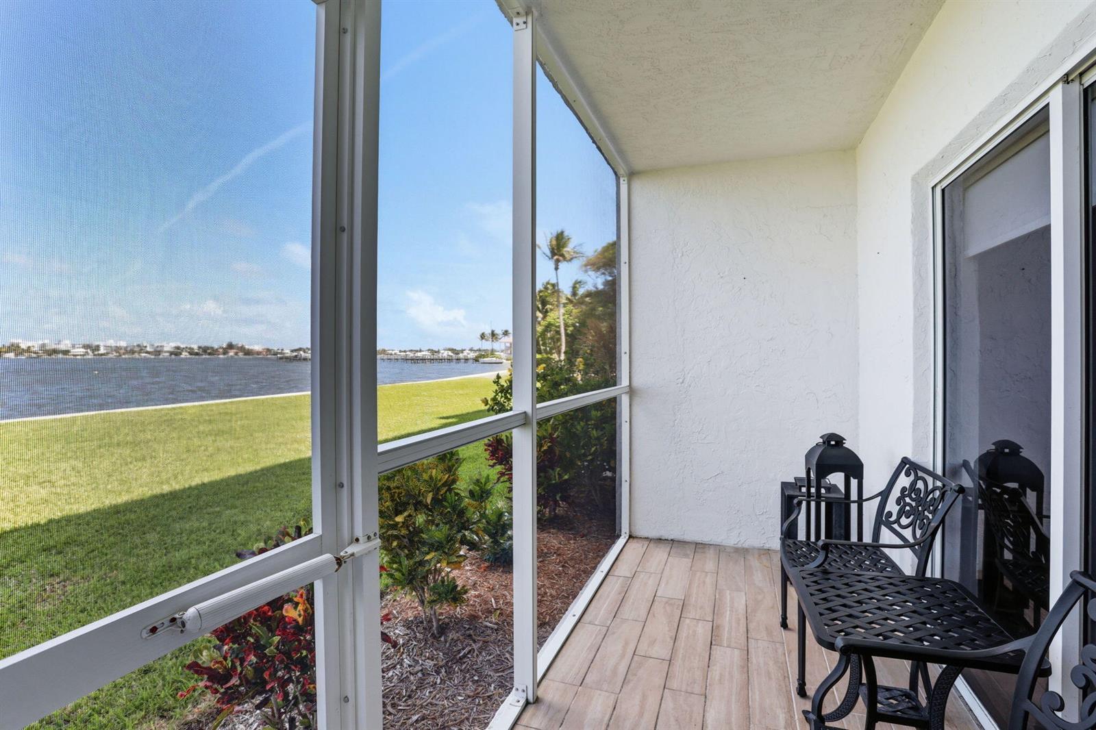 A screened-in balcony with tiled flooring overlooks a grassy lawn and a body of water — 1516 S Lakeside Drive # 103, FL 33460, FL