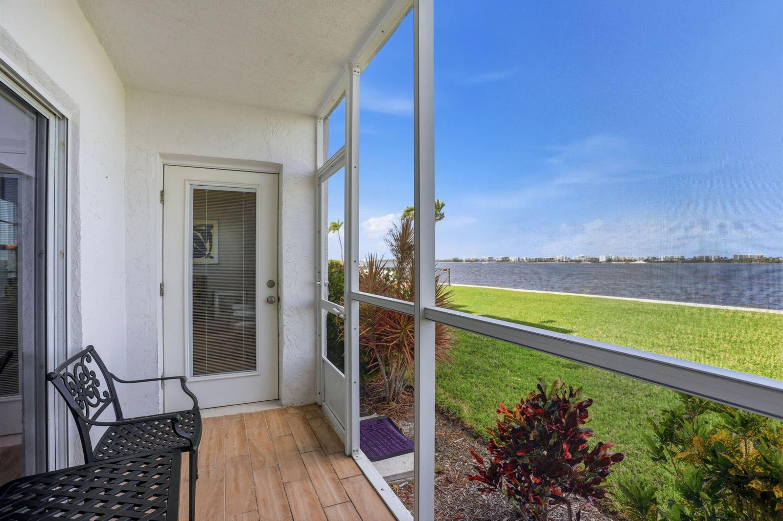 A screened-in balcony with tile flooring overlooks a grassy lawn and a body of water — 1516 S Lakeside Drive # 103, FL 33460, FL