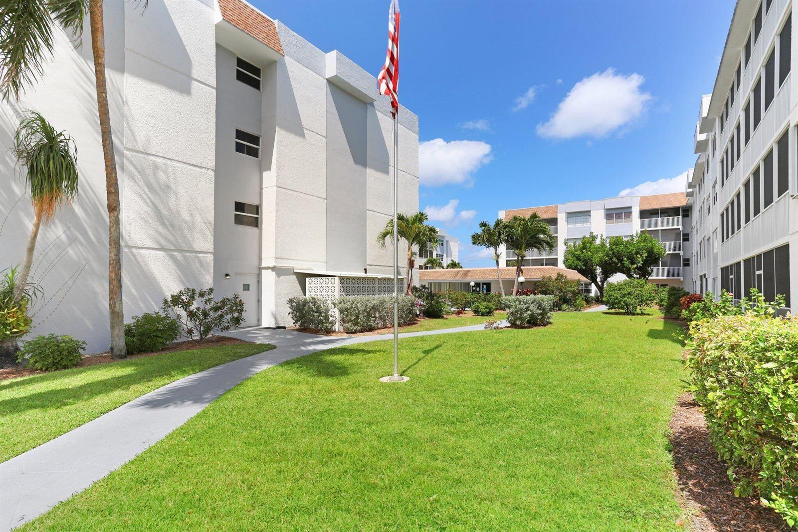 A grassy courtyard sits between two multi-story apartment buildings with a central flagpole — 1516 S Lakeside Drive # 103, FL 33460, FL