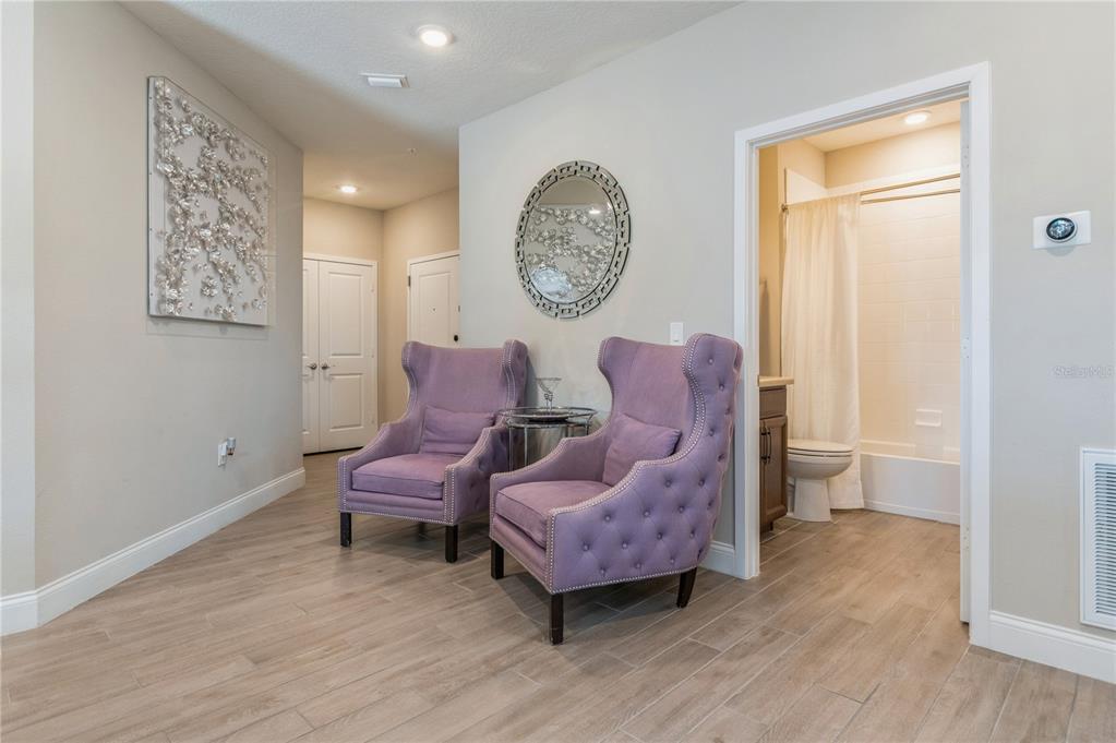 Two purple wingback chairs sit in a hallway with wood-look tile flooring and a bathroom — 7517 LAUREATE BOULEVARD UNIT 4103, ORLANDO, FL