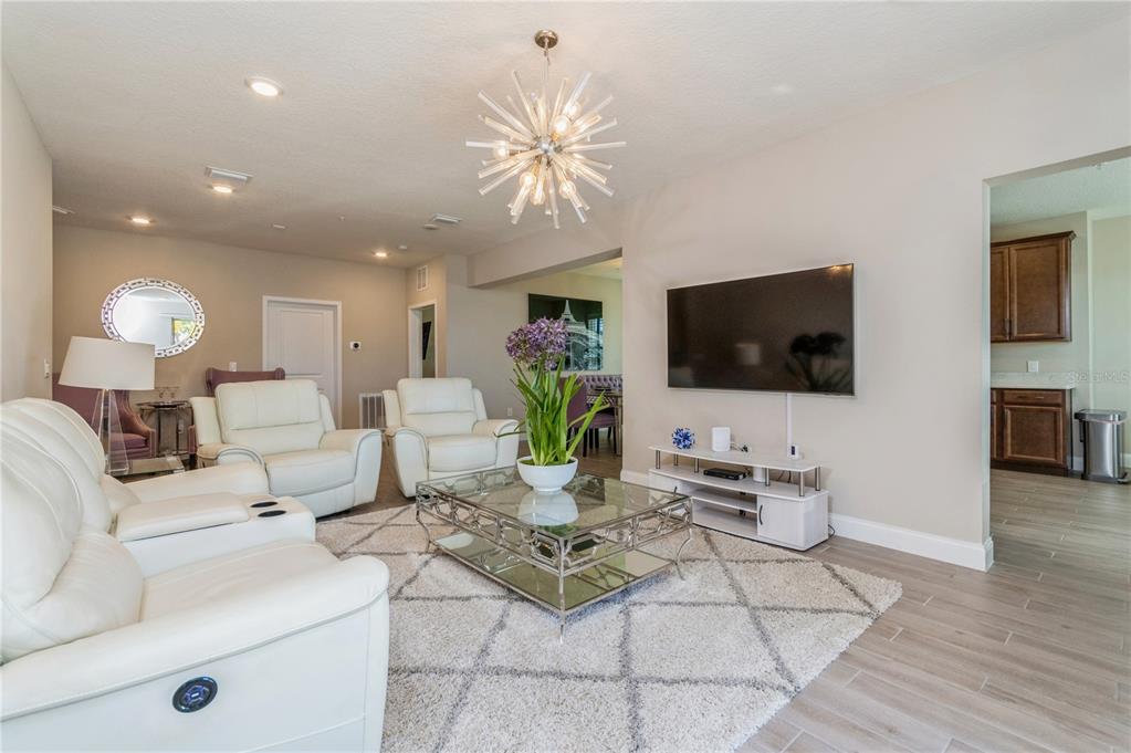 A living room features white leather furniture, a glass coffee table, and a starburst chandelier — 7517 LAUREATE BOULEVARD UNIT 4103, ORLANDO, FL