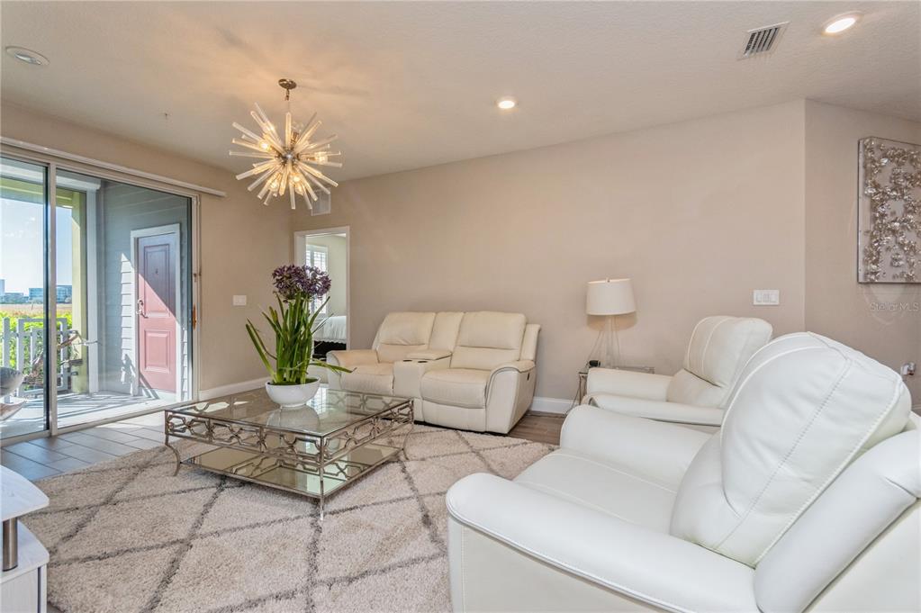 A living room features white leather seating, a glass coffee table, and a starburst chandelier — 7517 LAUREATE BOULEVARD UNIT 4103, ORLANDO, FL