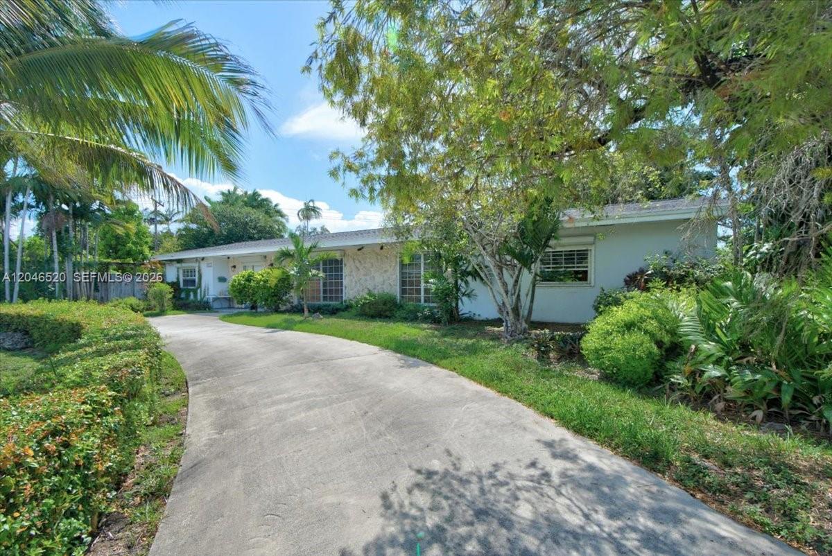 A single-story house with a concrete driveway, stone facade, and surrounding trees and landscaping — 9841 SW 157th Ter, Miami FL 33157, MIAMI, FL
