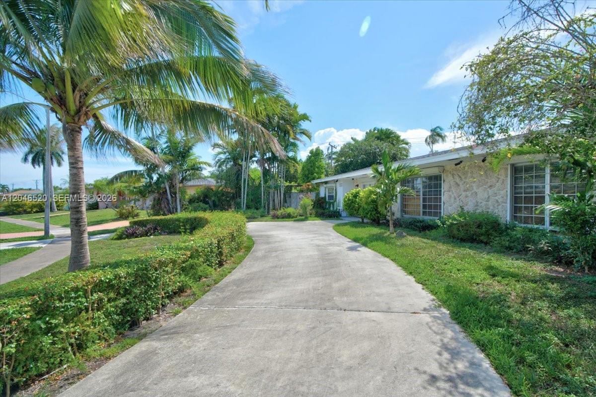 A concrete driveway leads to a one-story house with stone siding and palm trees — 9841 SW 157th Ter, Miami FL 33157, MIAMI, FL