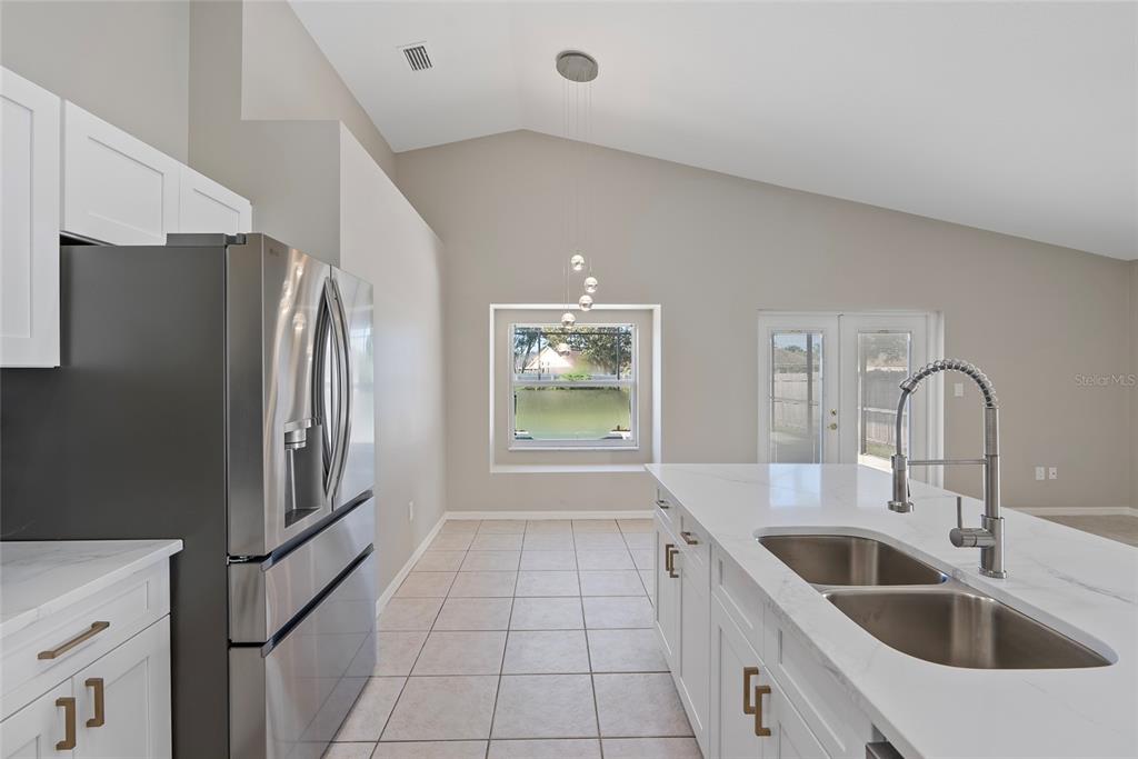 A kitchen features white cabinets, a stainless steel refrigerator, a quartz island, and tile flooring — 1831 ERIN BROOKE DRIVE, VALRICO, FL