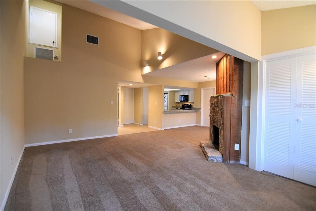 A living room with beige carpet, a stone fireplace, and an open kitchen in the background — 1068 E MICHIGAN STREET UNIT B, ORLANDO, FL