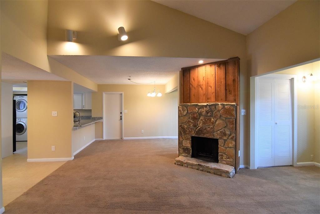 A living room features a stone fireplace, vaulted ceilings, beige carpeting, and an adjacent kitchen — 1068 E MICHIGAN STREET UNIT B, ORLANDO, FL