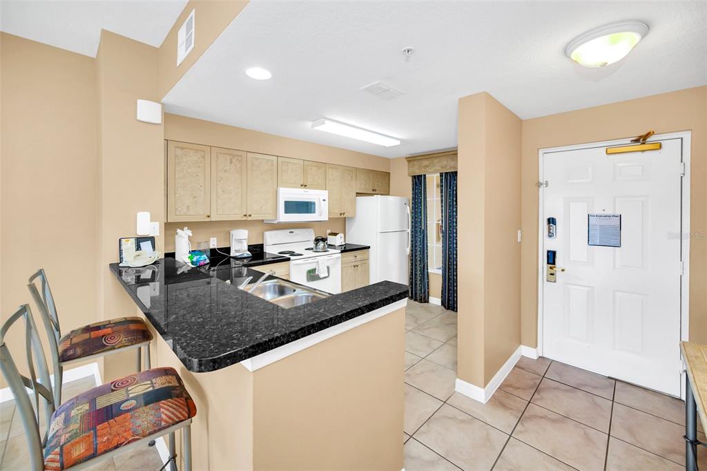 A kitchen with light wood cabinets, black granite countertops, and a breakfast bar with stools — 8815 WORLDQUEST BOULEVARD UNIT 2403, ORLANDO, FL
