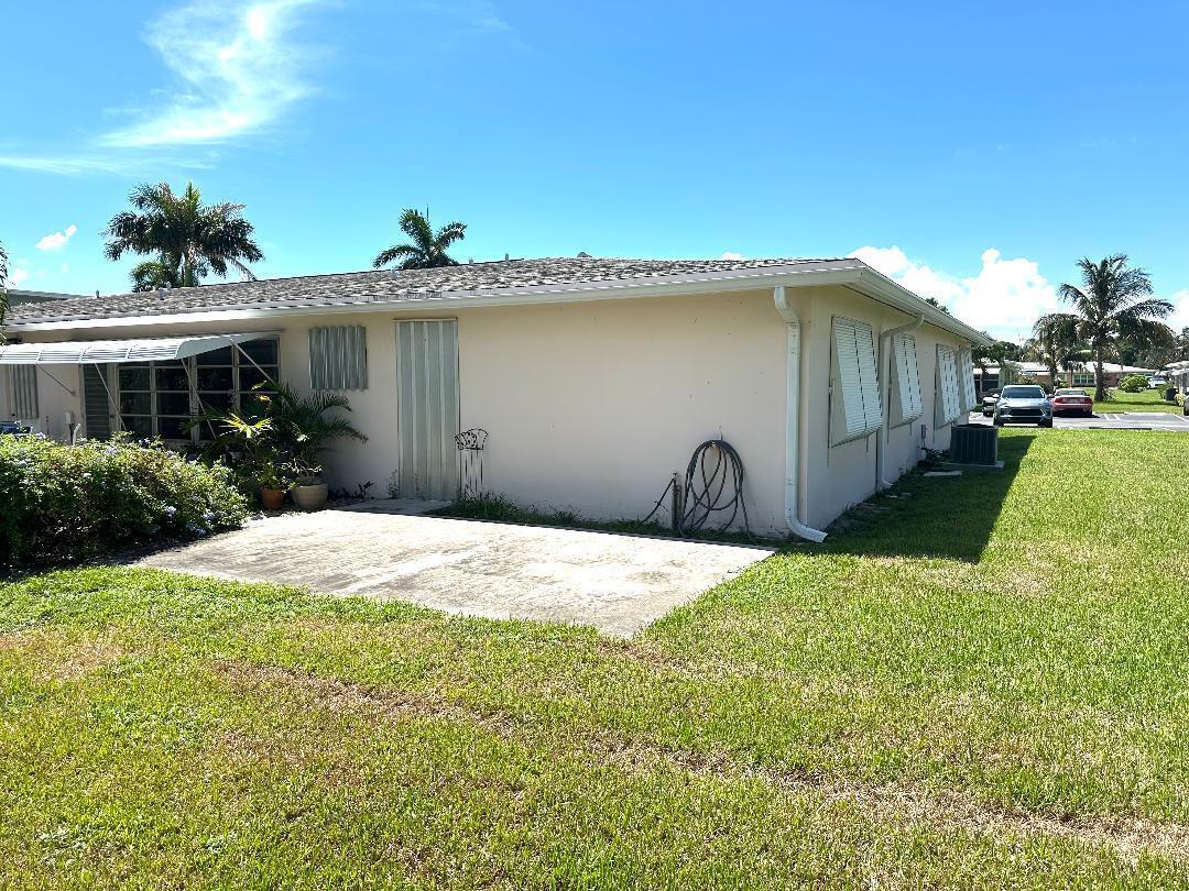 The exterior of a single-story house features a concrete patio, lawn, and metal shutters — 135 South Boulevard # A, Boynton Beach FL 33435, BOYNTON BEACH, FL