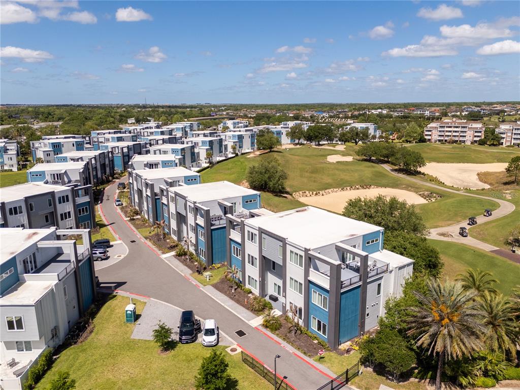 An aerial view shows modern multi-story apartment buildings situated next to a golf course — 7740 SANDY RIDGE DRIVE UNIT 247, REUNION, FL