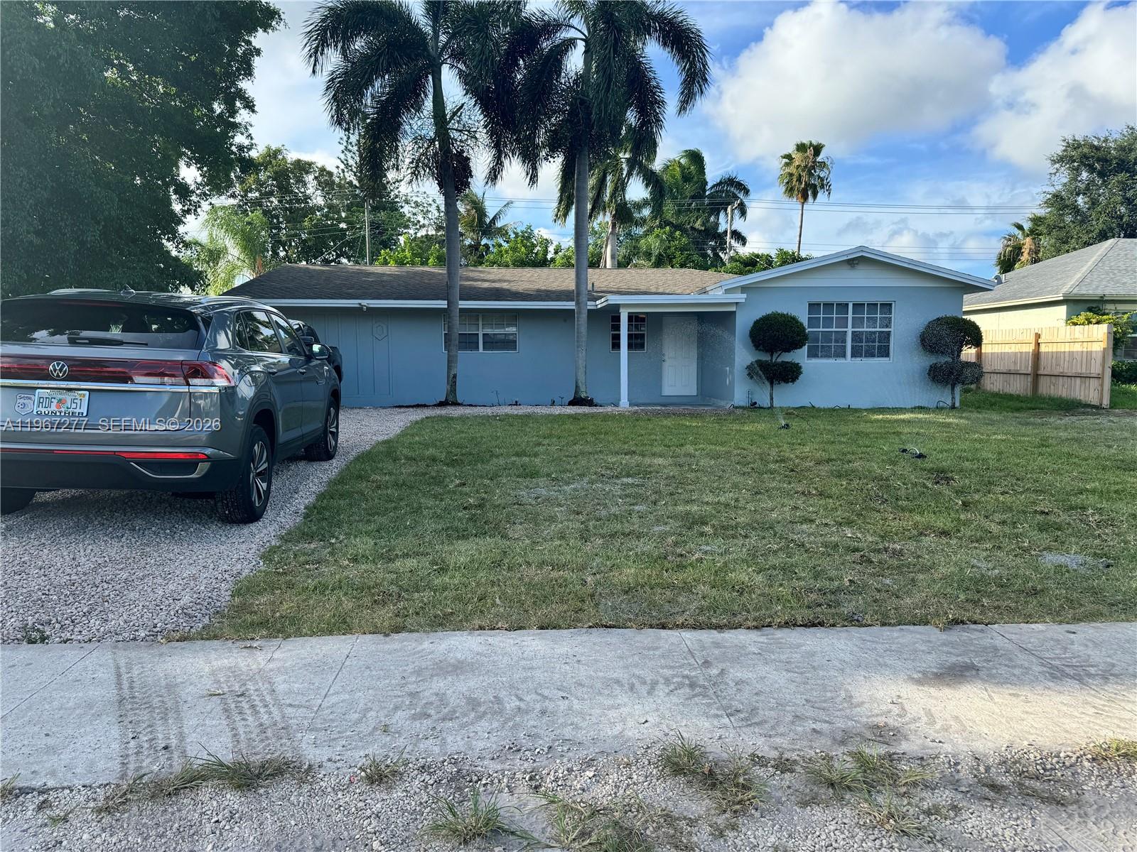 A light blue single-story house features a gravel driveway, palm trees, and a front lawn — 4381 Purdy Ln, West Palm Beach FL 33406, WEST PALM BEACH, FL