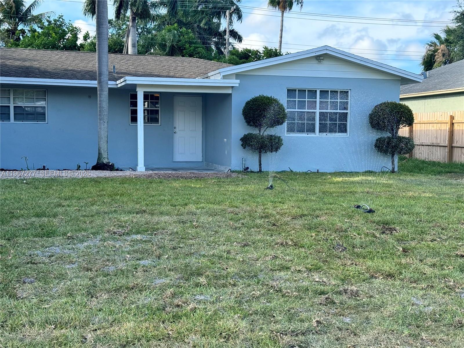 A light blue single-story house features a covered entryway, white trim, and two manicured shrubs — 4381 Purdy Ln, West Palm Beach FL 33406, WEST PALM BEACH, FL