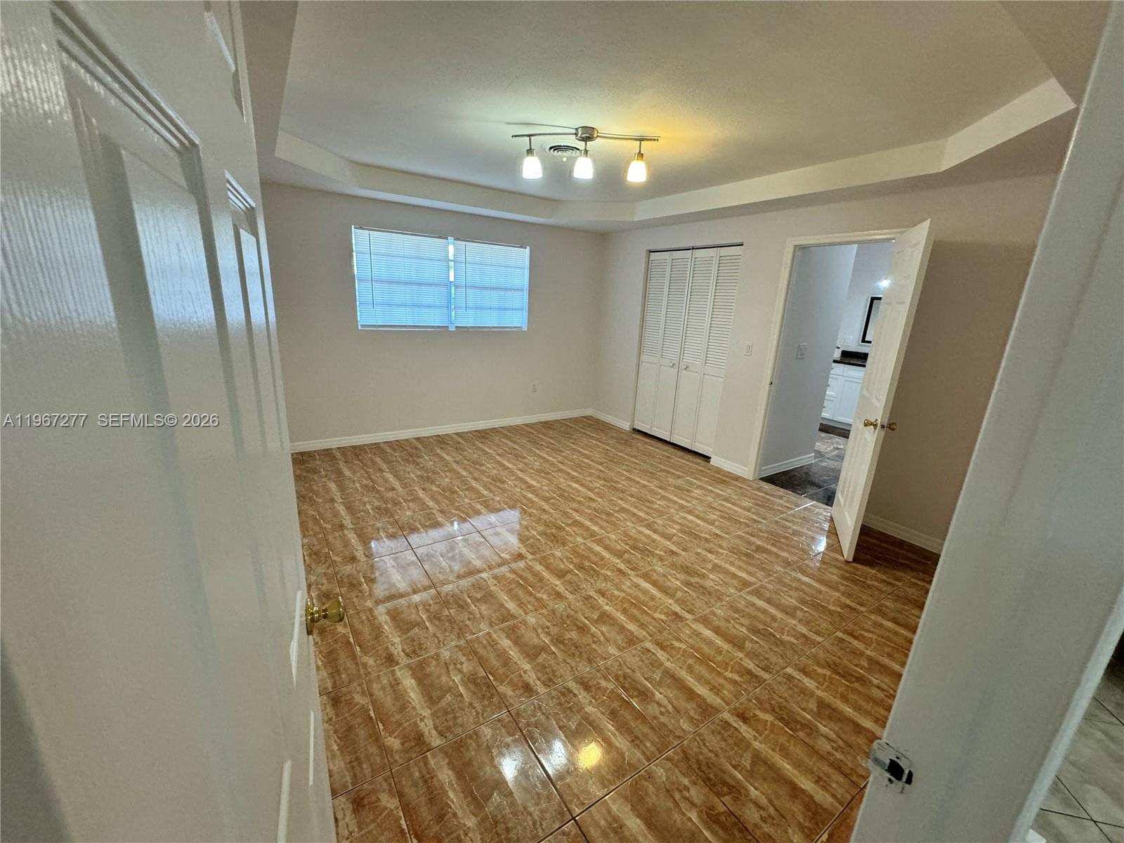 An empty bedroom features tan tile flooring, a tray ceiling, and a white closet — 4381 Purdy Ln, West Palm Beach FL 33406, WEST PALM BEACH, FL